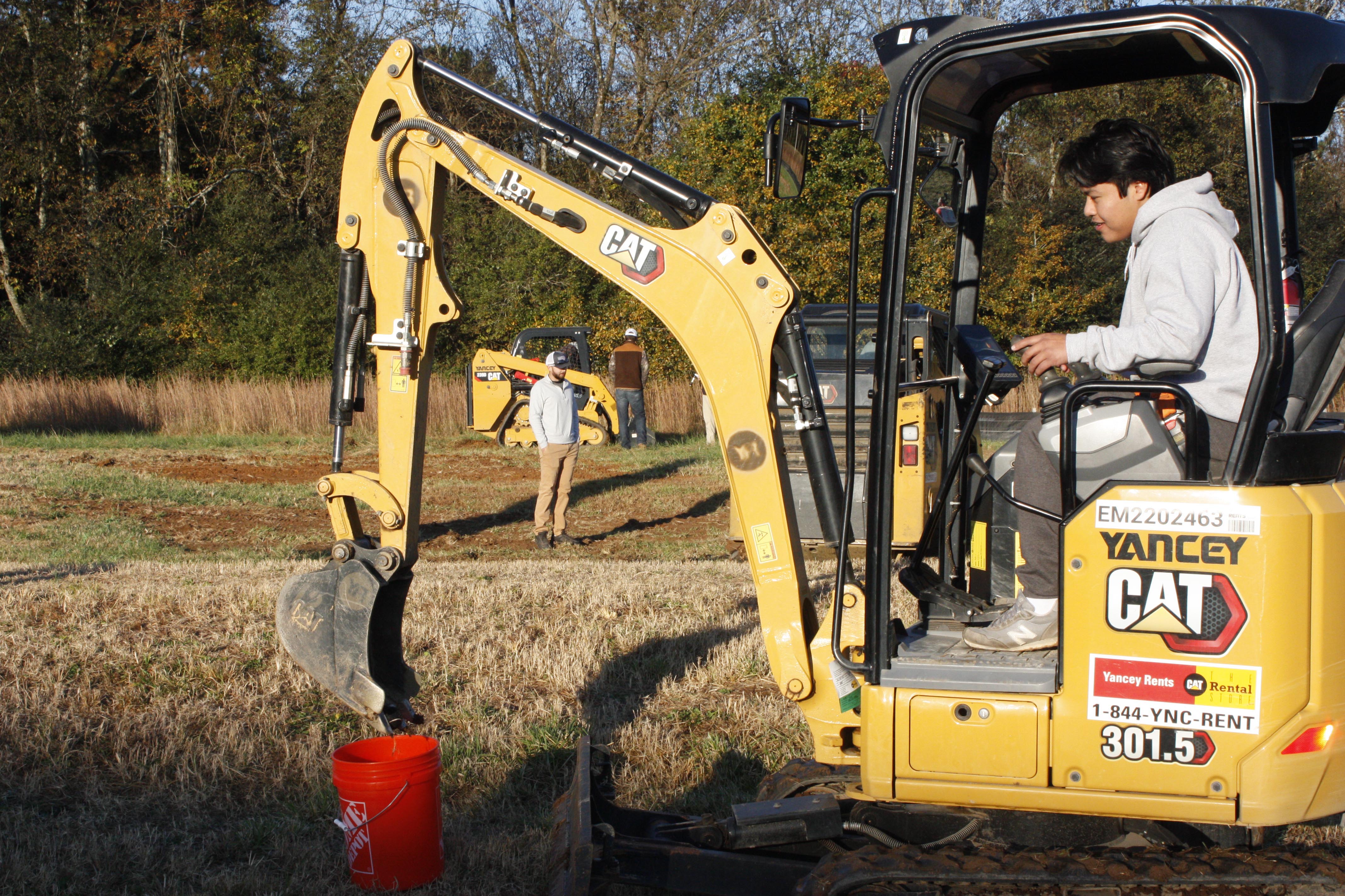 GNTC student Alfredo Perez manipulates the bucket of a mini-excavator to scoop up a small ball and drop it into a bucket in a timed competition.