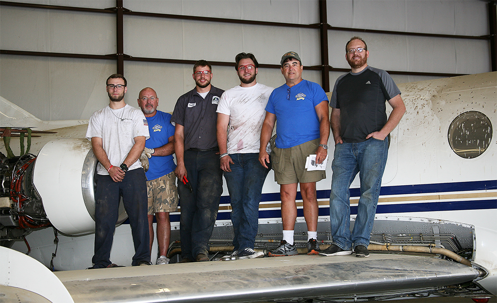 (From left to right), Greg Merwitz of Rome, GNTC Aviation Maintenance Technology student; Monty Montague, project partner; Cody West of Newnan, GNTC Aviation Maintenance Technology student; Nick Martin of Newnan, GNTC Aviation Maintenance Technology student; Sam Edwards, owner of Sam’s Burger-Deli/Schroder’s; and Stephen Griffin, Aviation Maintenance Technology instructor at GNTC, stand on the wing of the Dassault Falcon 20 business jet.