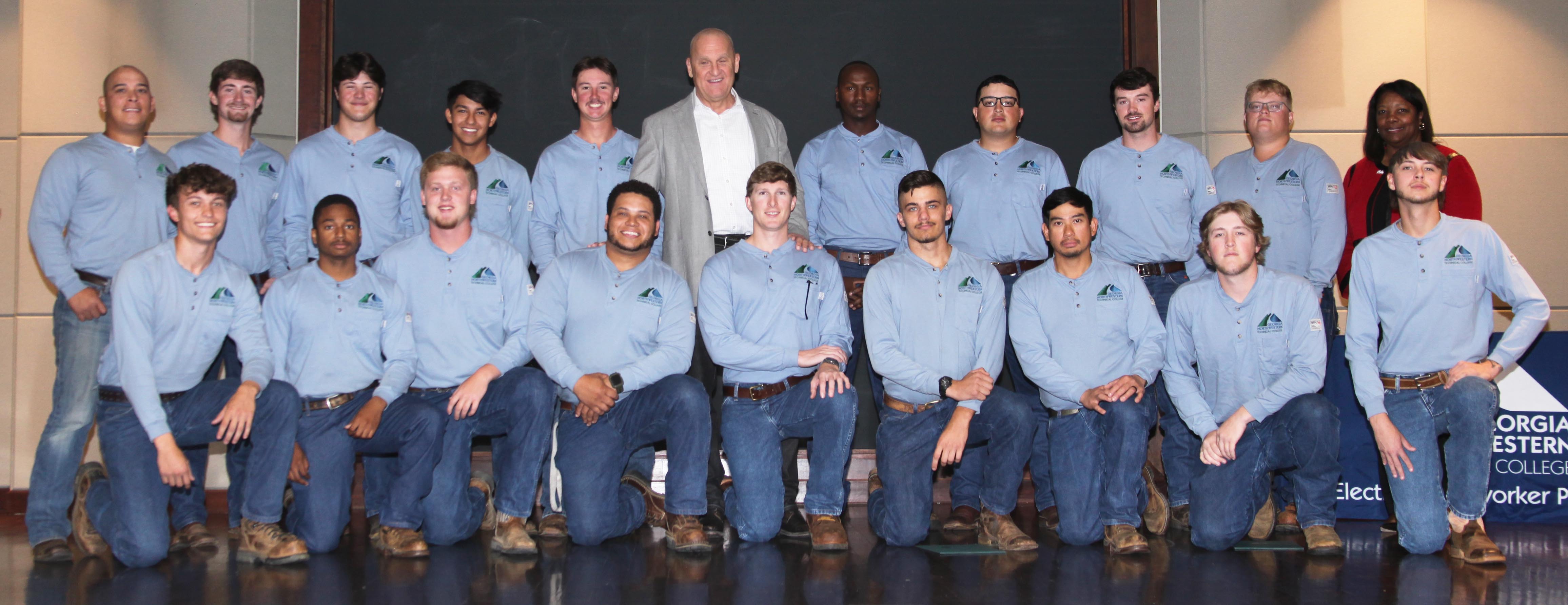 The first cohort of students graduate from GNTC’s Electrical Lineworker Program (from left, kneeling) William Bryce Epperson, Malik Reese, Ethan Tucker, Joshua Daum, Jonathan Hood, Isaac Ritter, Glenn Jose, Rylan McAlister, Brent Gentry; (standing) Melvin Pledger III, Logan Davenport, Chandler Caleb Hall, Cesar Molina, Josh Adams, Alabama Power Executive Vice President of Customer and Employee Services Jeff Peoples, Cosmas Kipruto, Salvador Barragan, Christopher (Ross) Moore, Jaylen Larkin and Georgia Power Senior Vice President of Power Delivery Fran Forehand.